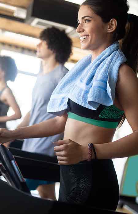 Woman on a treadmill smiling with a towel around her neck.